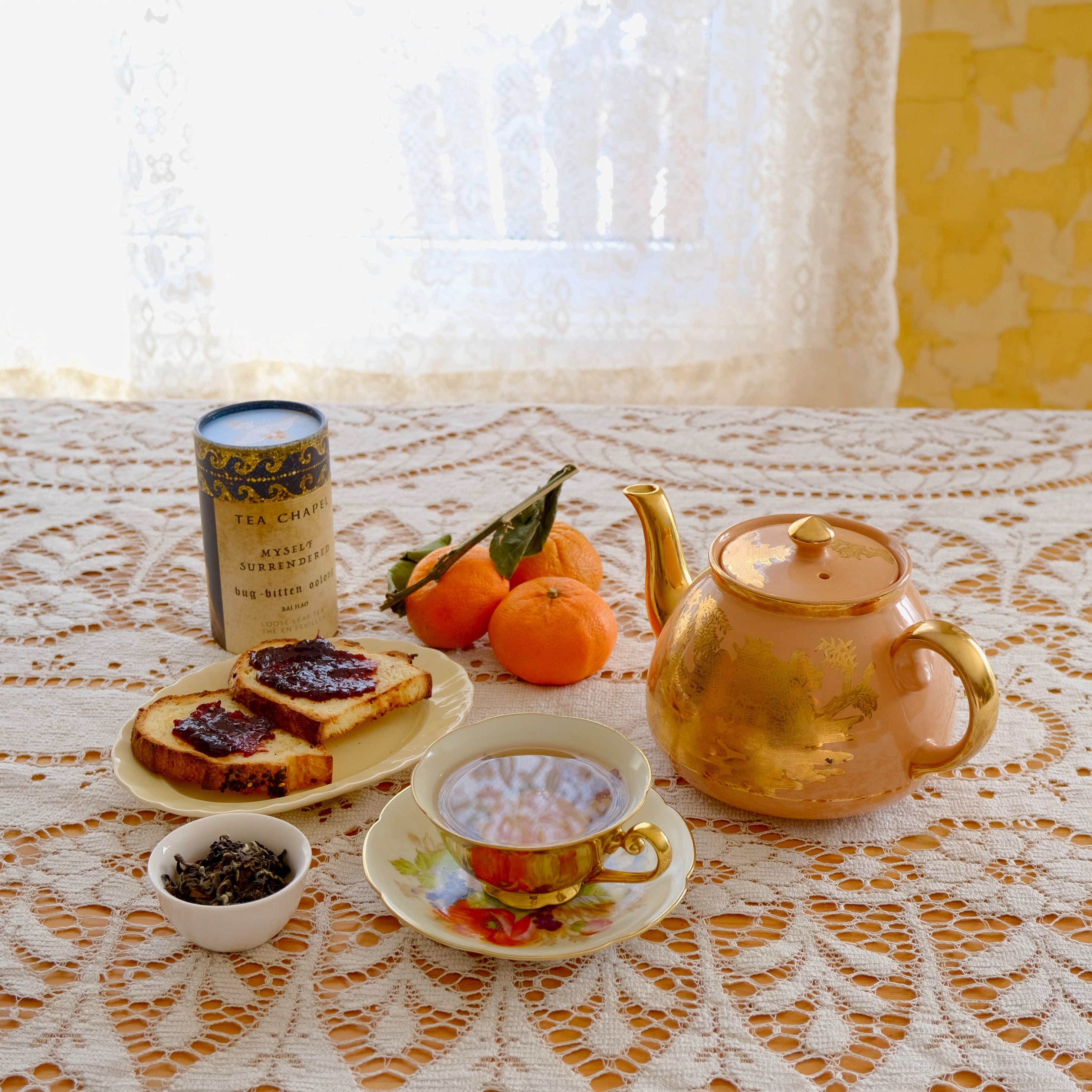 Tea set with a teapot, cups, and snacks on a lace tablecloth.