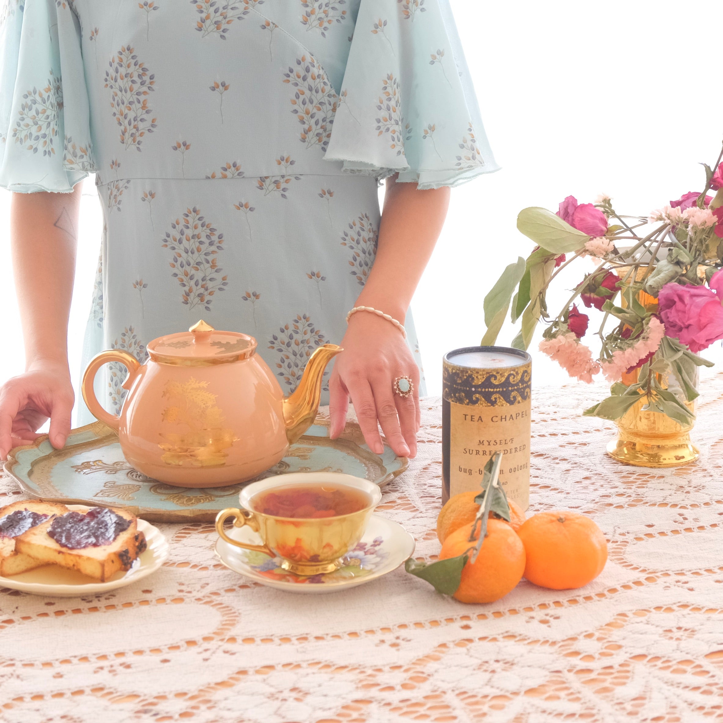 Tea set with a teapot, cup, and plate on a table with a person partially visible.