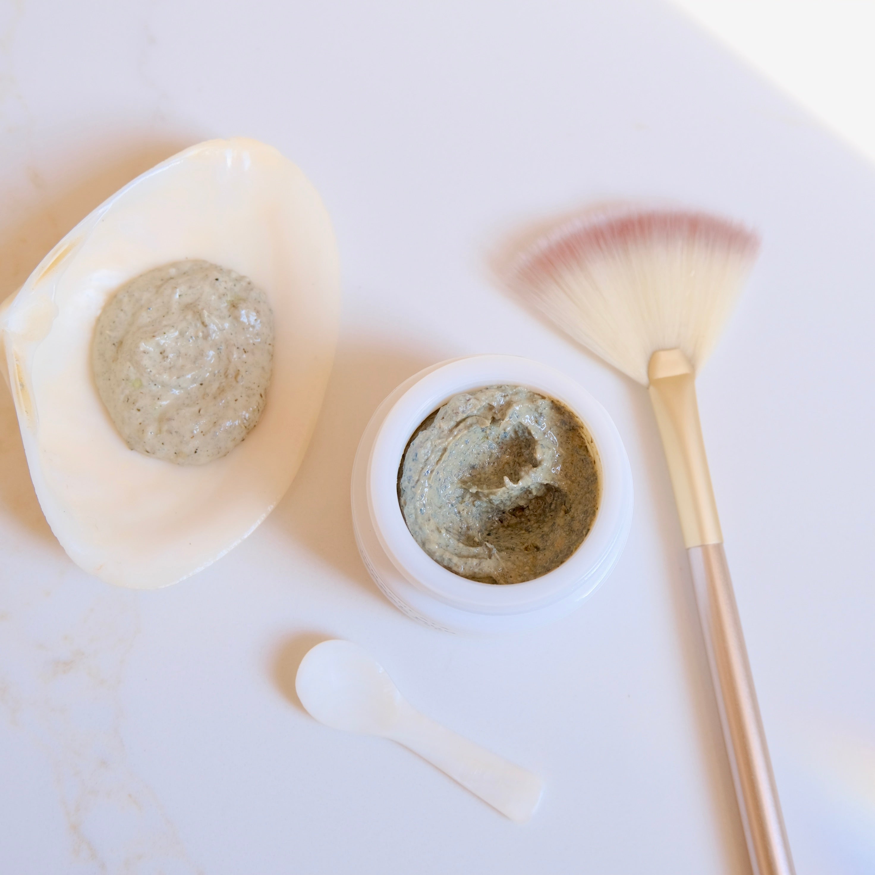 Two containers of green clay product with a brush on a white surface