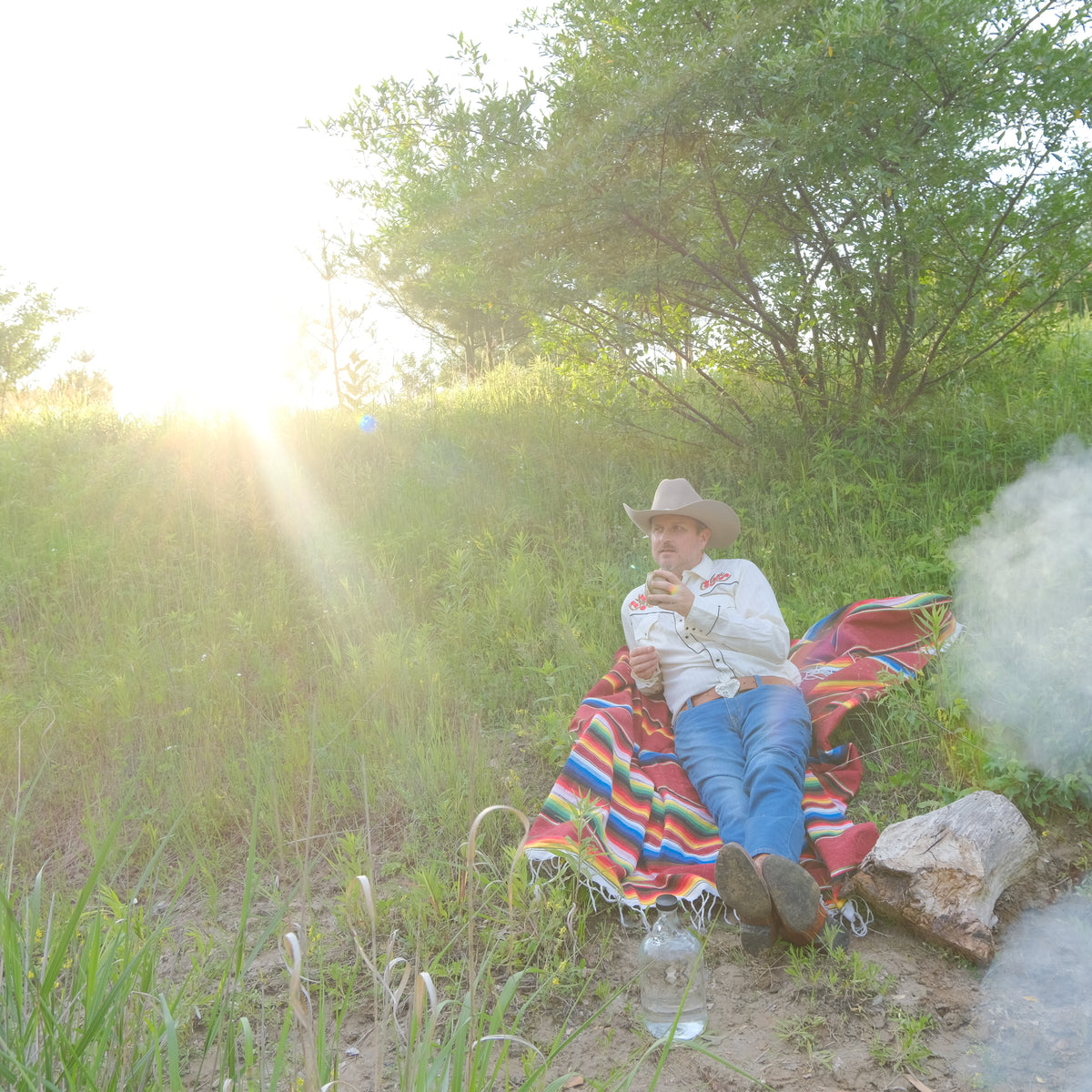 Person sitting on a colorful blanket in a natural setting with trees and sunlight.