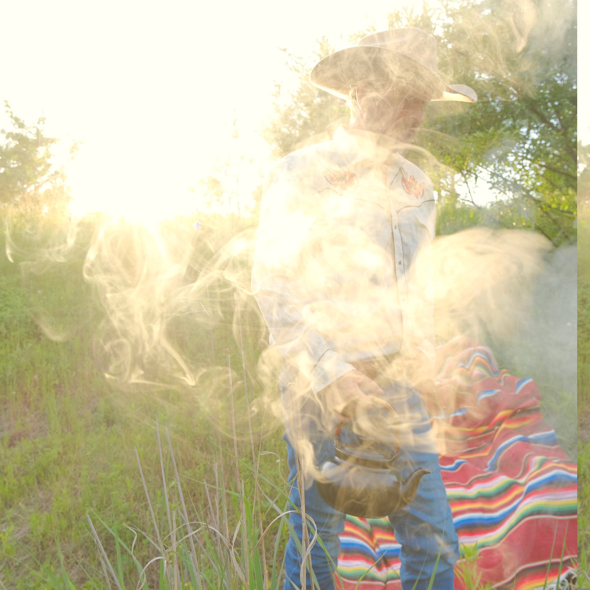 A cowboy making coffee, standing in a grassy field with smoke or mist around them.