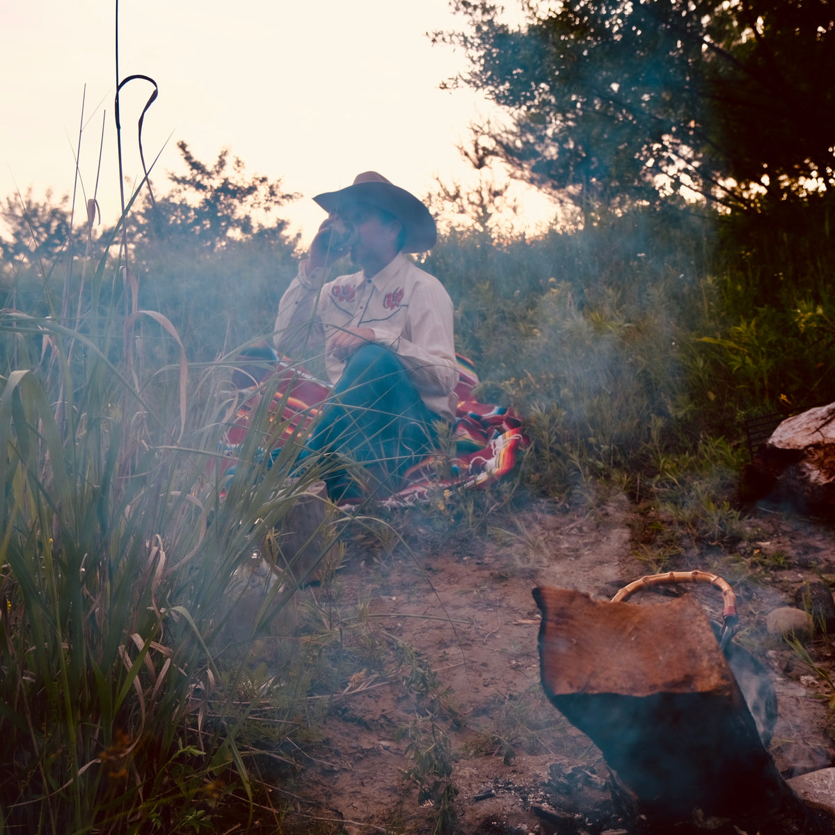 Person sitting by a campfire in a natural setting with a dog nearby