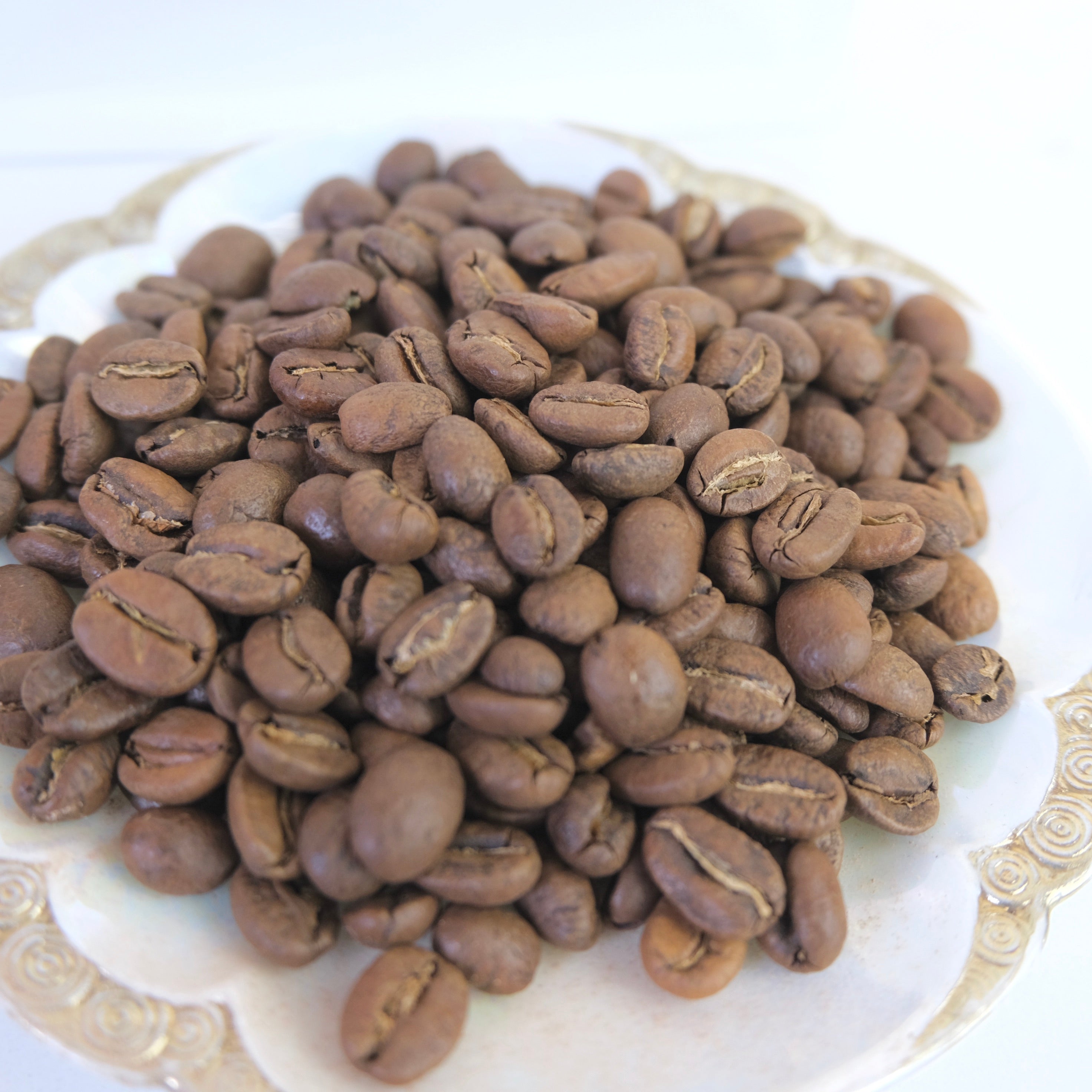 Coffee beans on a decorative white plate with gold rim