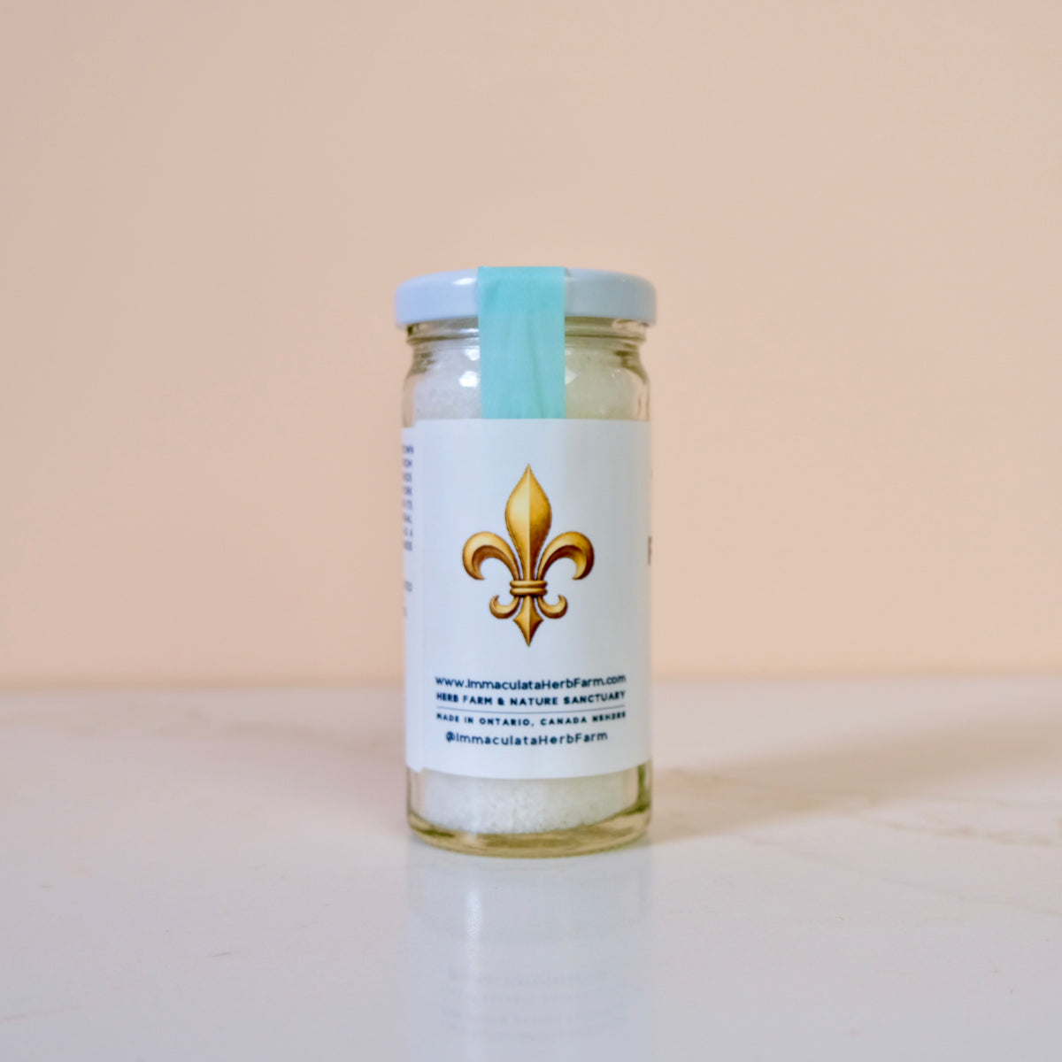 Glass jar with a white label featuring a gold fleur-de-lis on a beige background