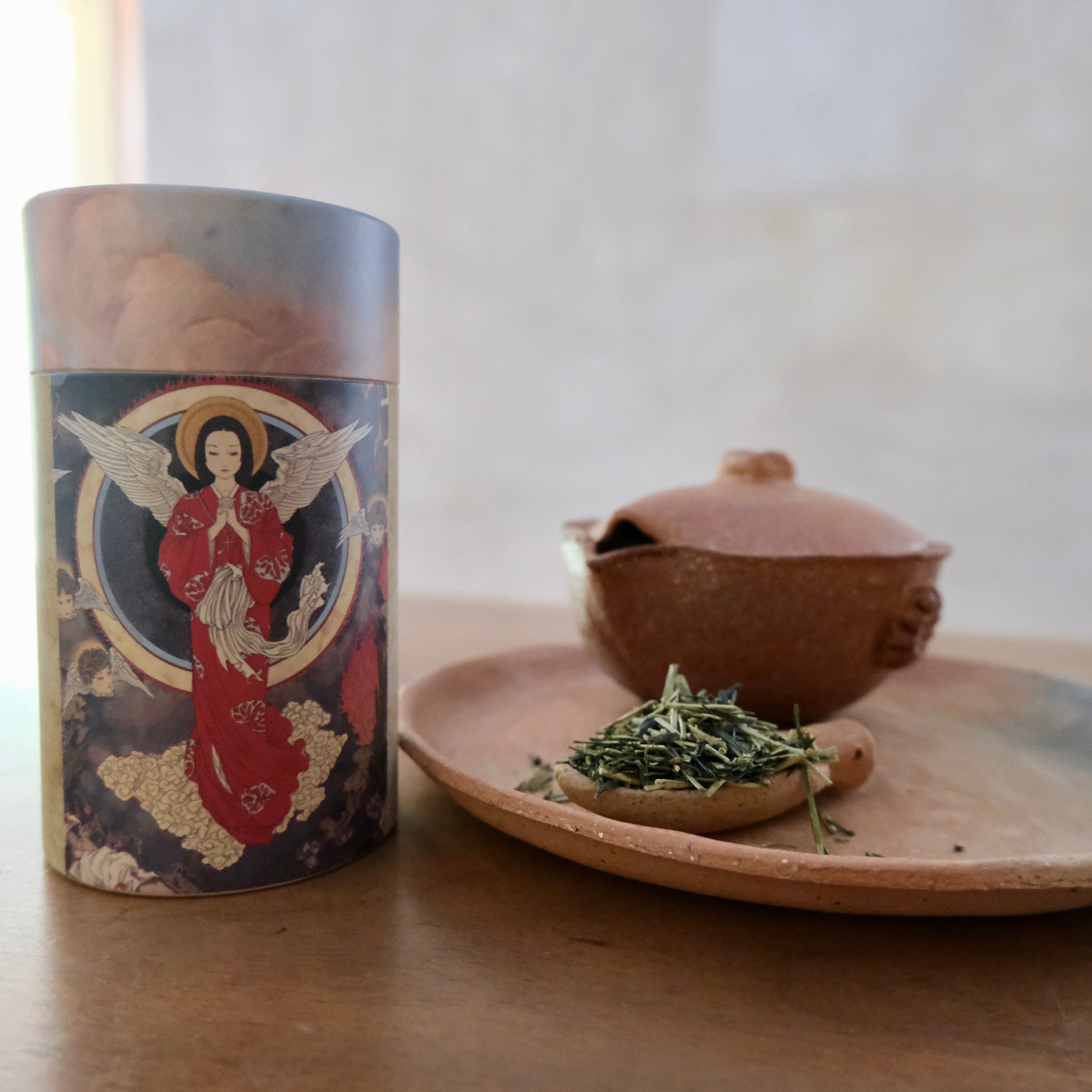 Tea canister with decorative label next to a wooden bowl with tea leaves on a wooden surface.