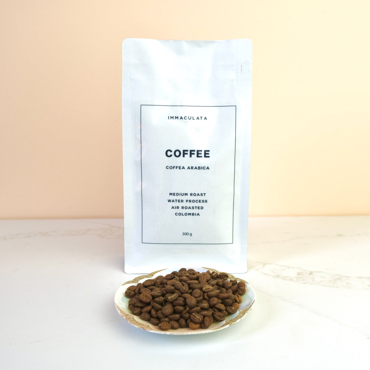Coffee beans on a plate with a white bag labeled 'Immaculata Coffee' in the background.