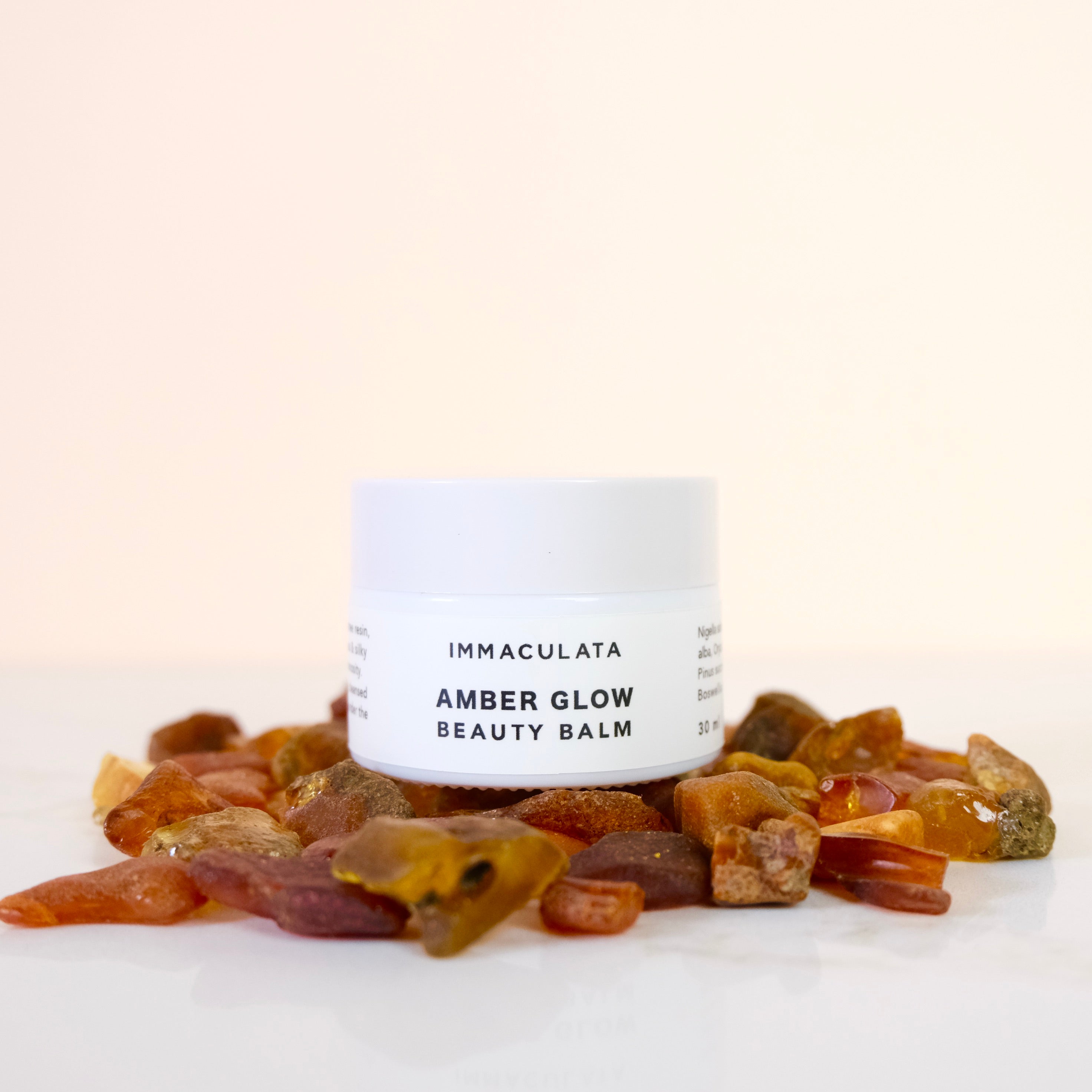 Amber glow beauty balm with amber stones on a white background