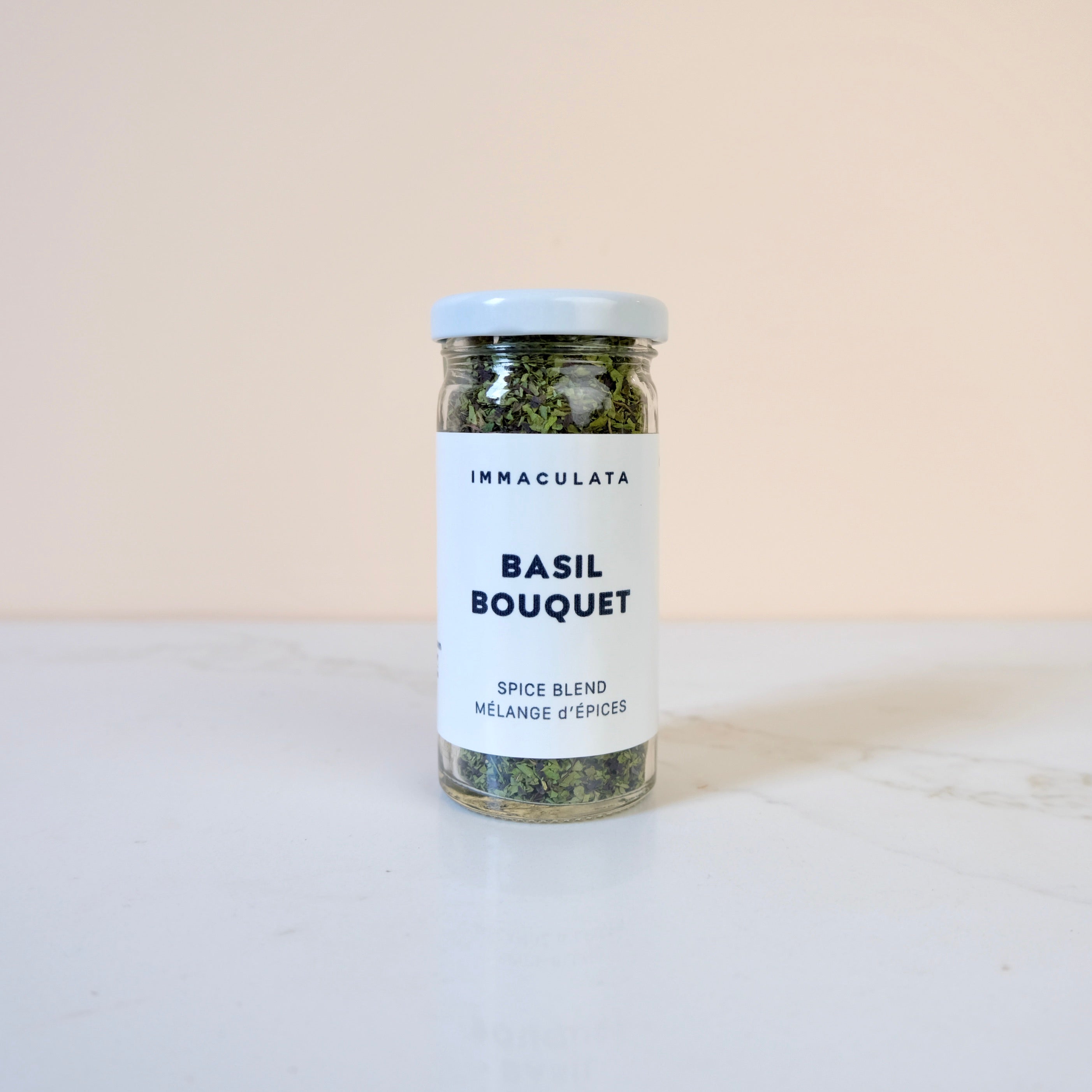 Jar of basil bouquet spice blend on a white surface with a beige background