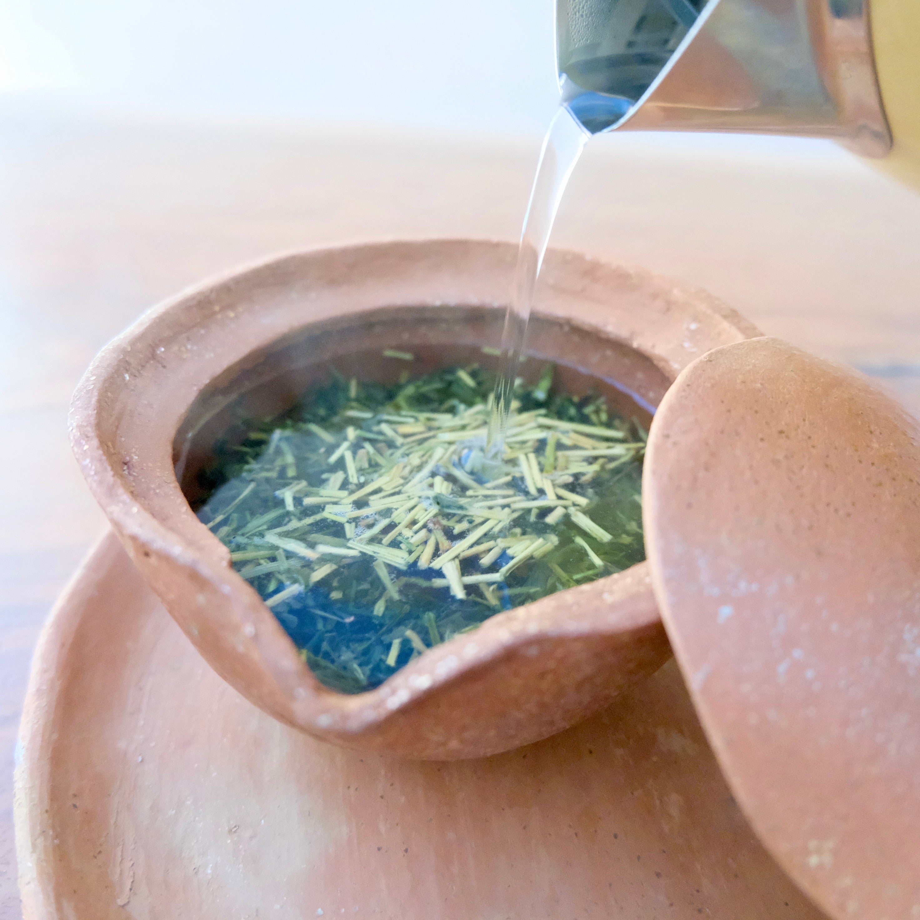 Tea leaves being poured into a ceramic teapot with a lid.