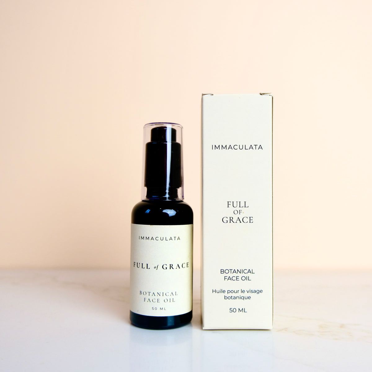 A bottle of IMMACULATA Full of Grace Botanical Face Oil next to its cream-colored product box, set against a soft beige background.