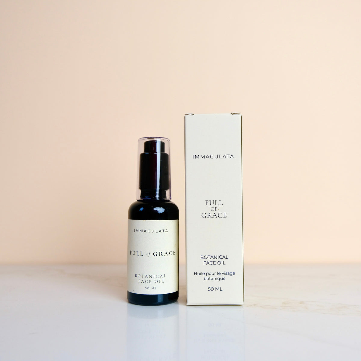 A bottle of Immaculata Full of Grace Botanical Face Oil next to its cream-colored packaging box, set against a soft beige background.