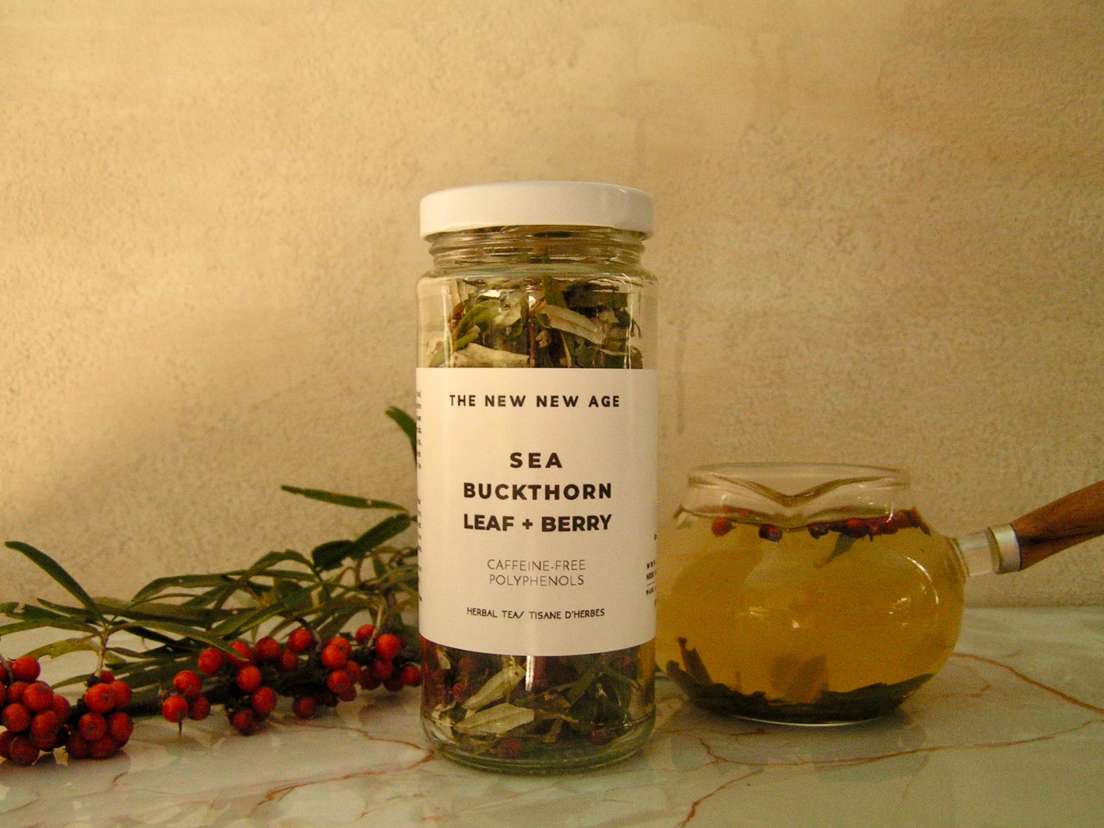 Jar of sea buckthorn leaf and berry with a label on a marble surface.