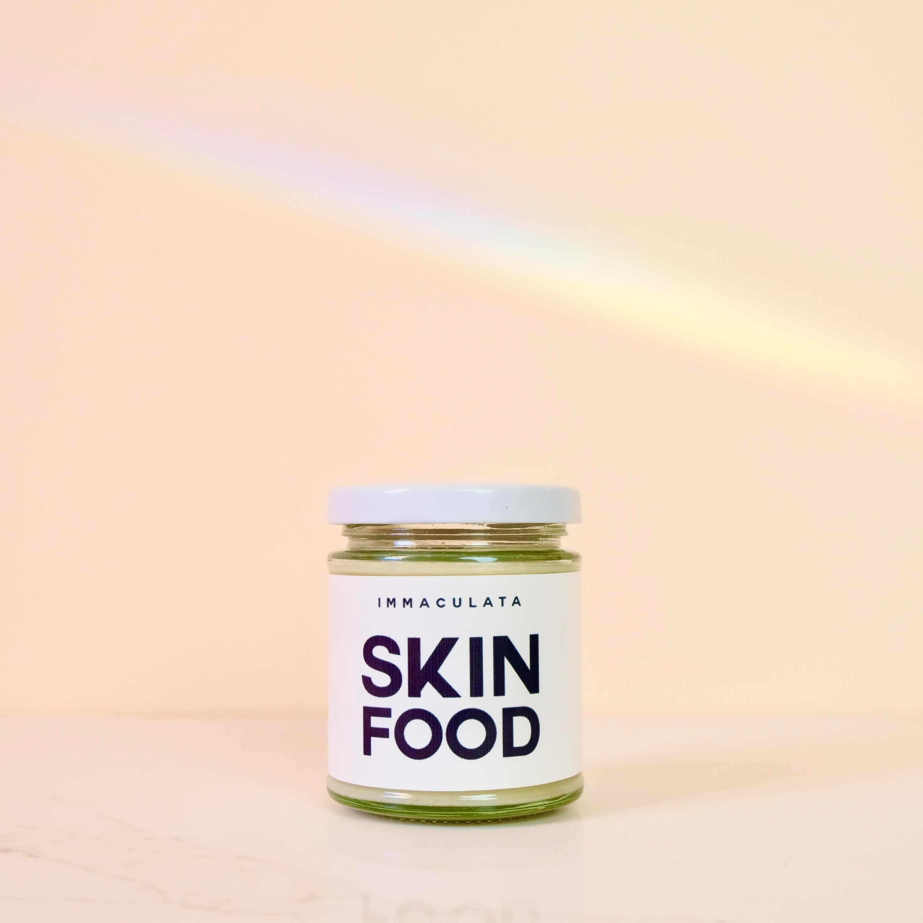 Jar of 'IMMACULATA Skin Food' on a beige background