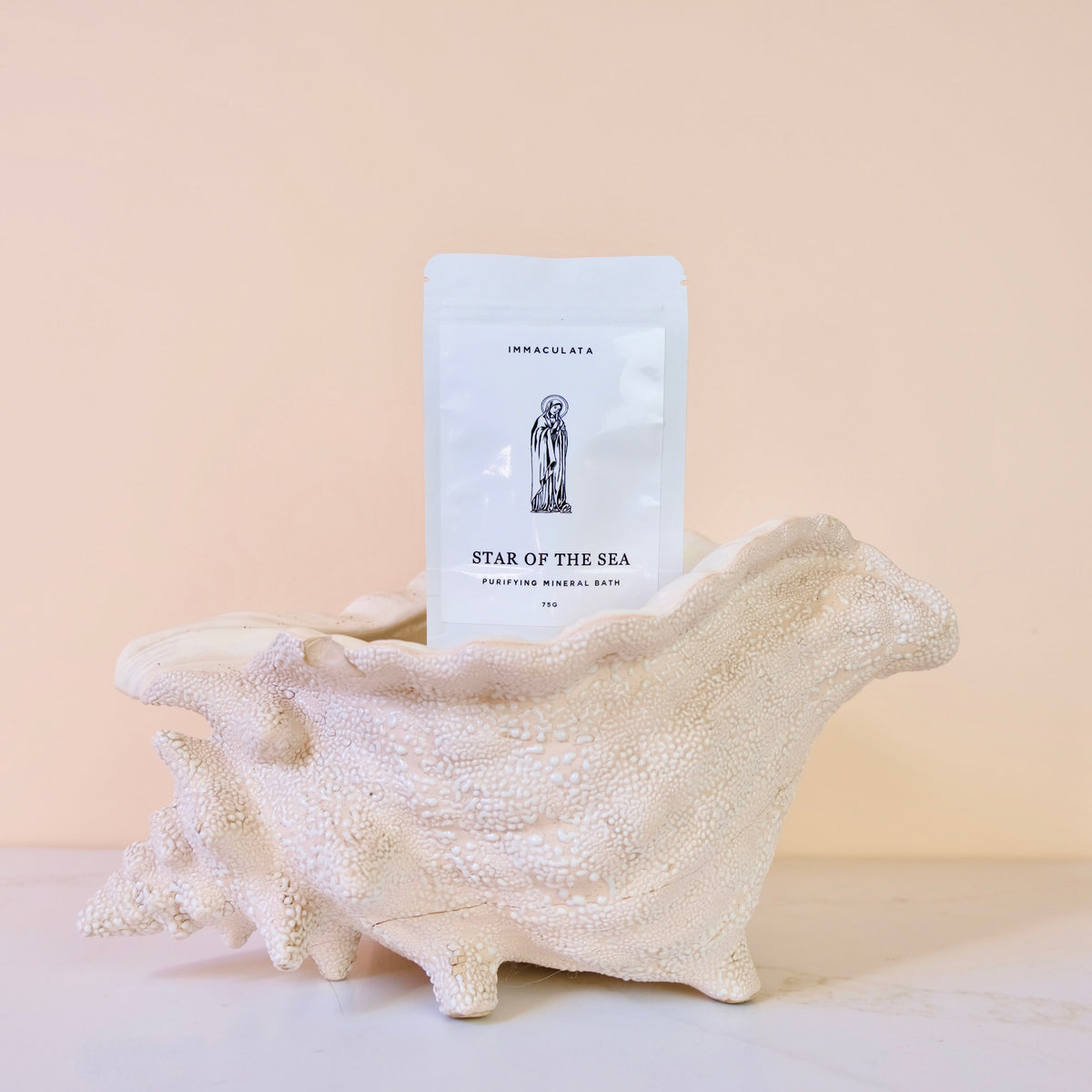 A white stand-up pouch labeled 'IMMACULATA STAR OF THE SEA' is displayed in front of a large white seashell on a pale beige background.