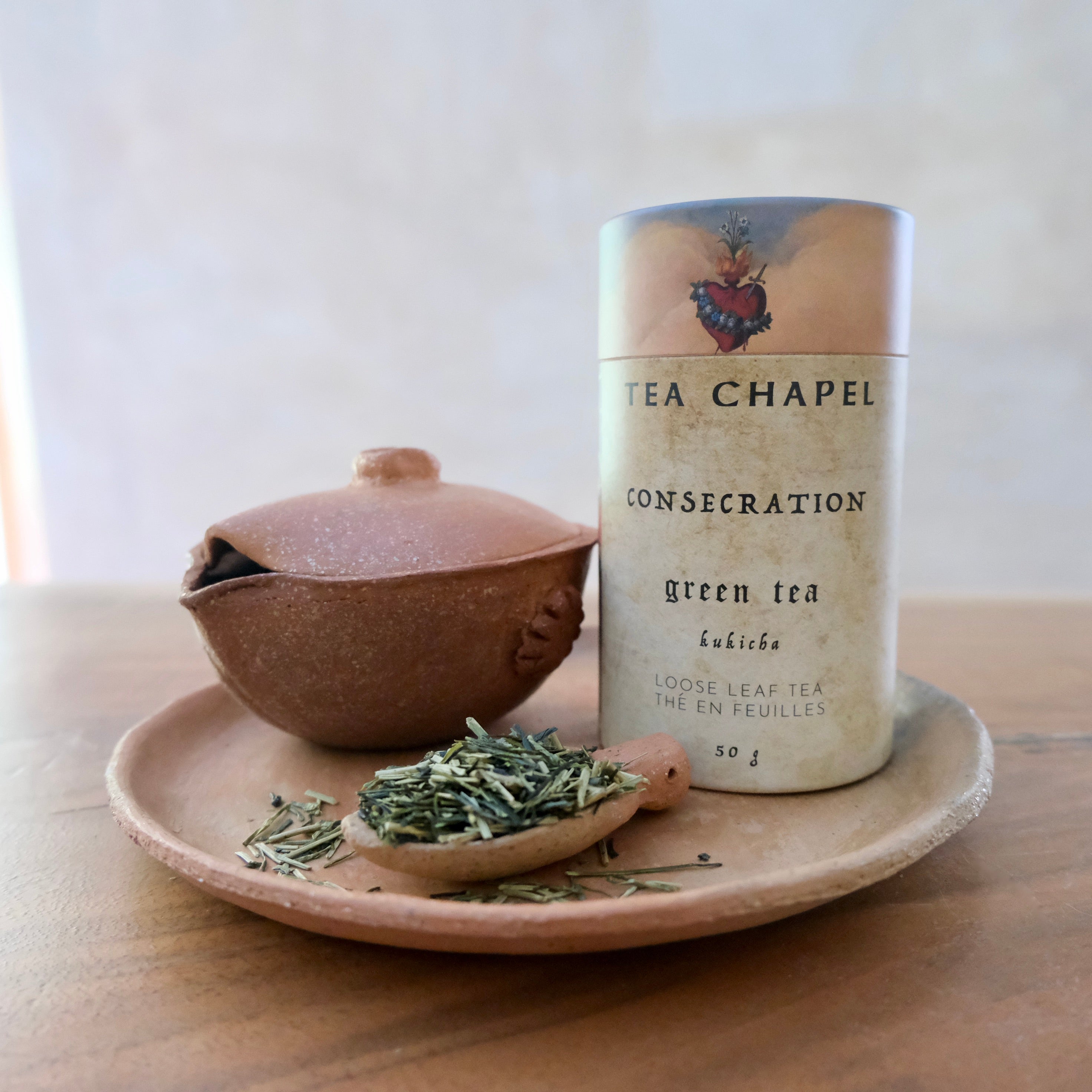 Tea canister labeled 'Tea Chapel' with a ceramic teapot and saucer on a wooden surface.