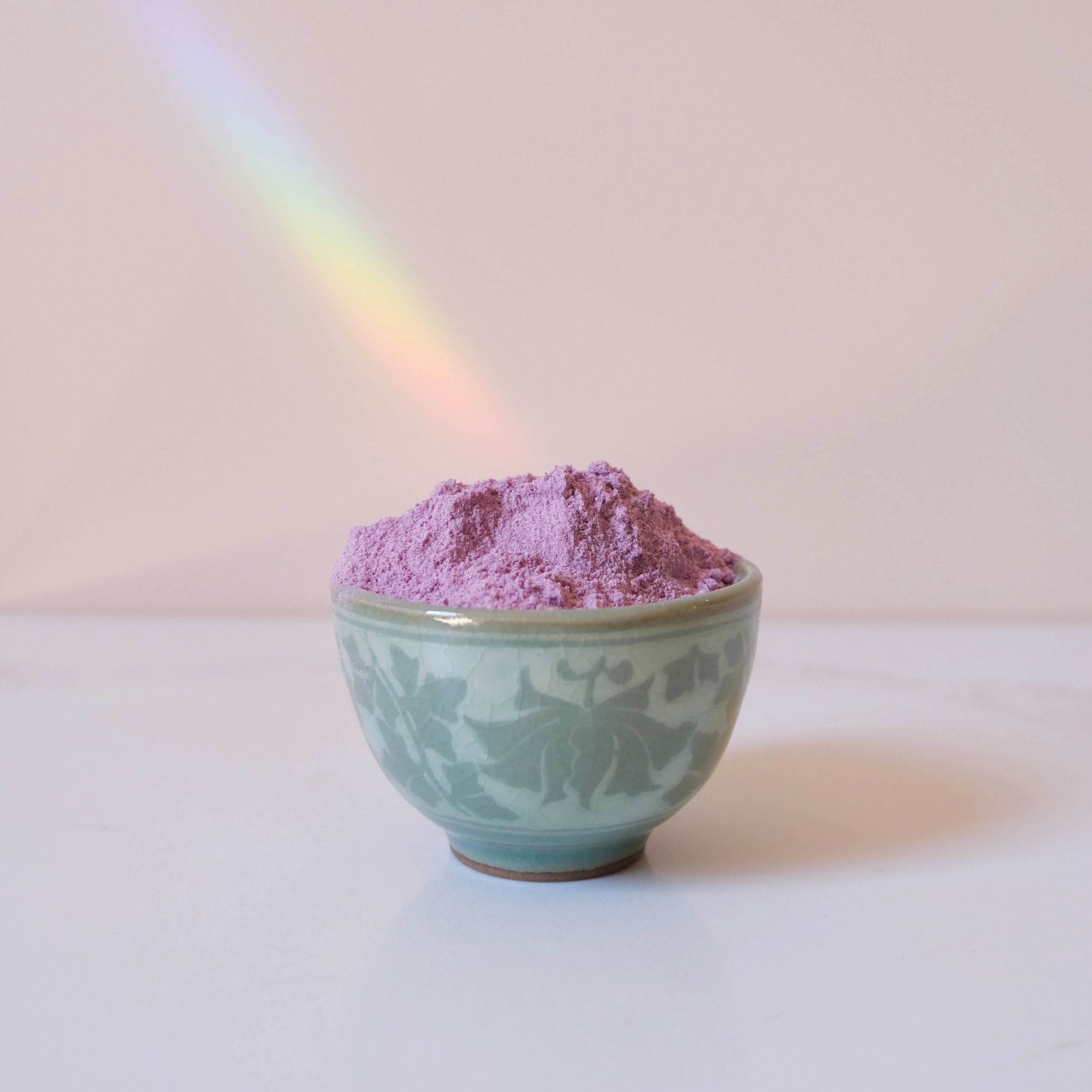 Bowl of purple ube powder with a rainbow in the background