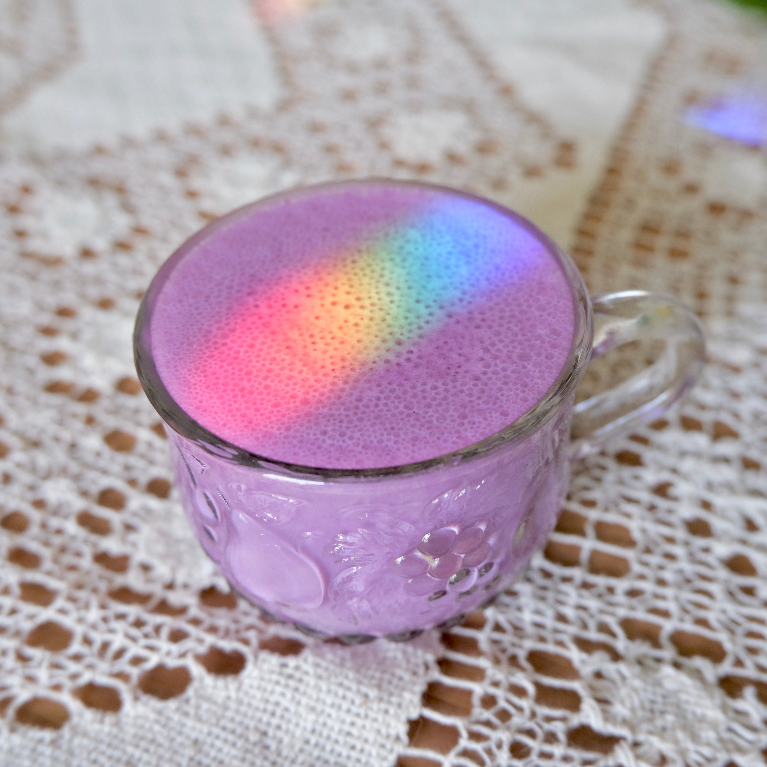 Glass mug with colorful ube foam on a lace tablecloth