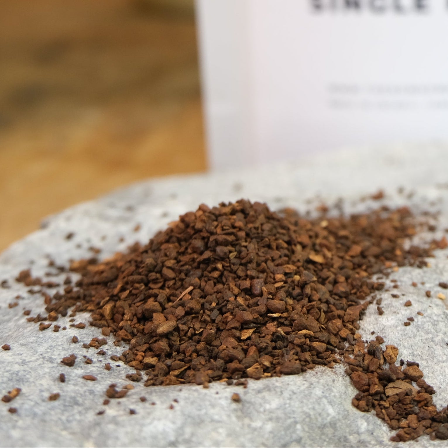 A package labeled 'ROASTED CHICORY ROOT' by 'The New New Age' with a pile of brown chicory root pieces in front of it, placed on a wooden surface with a plant in the background.